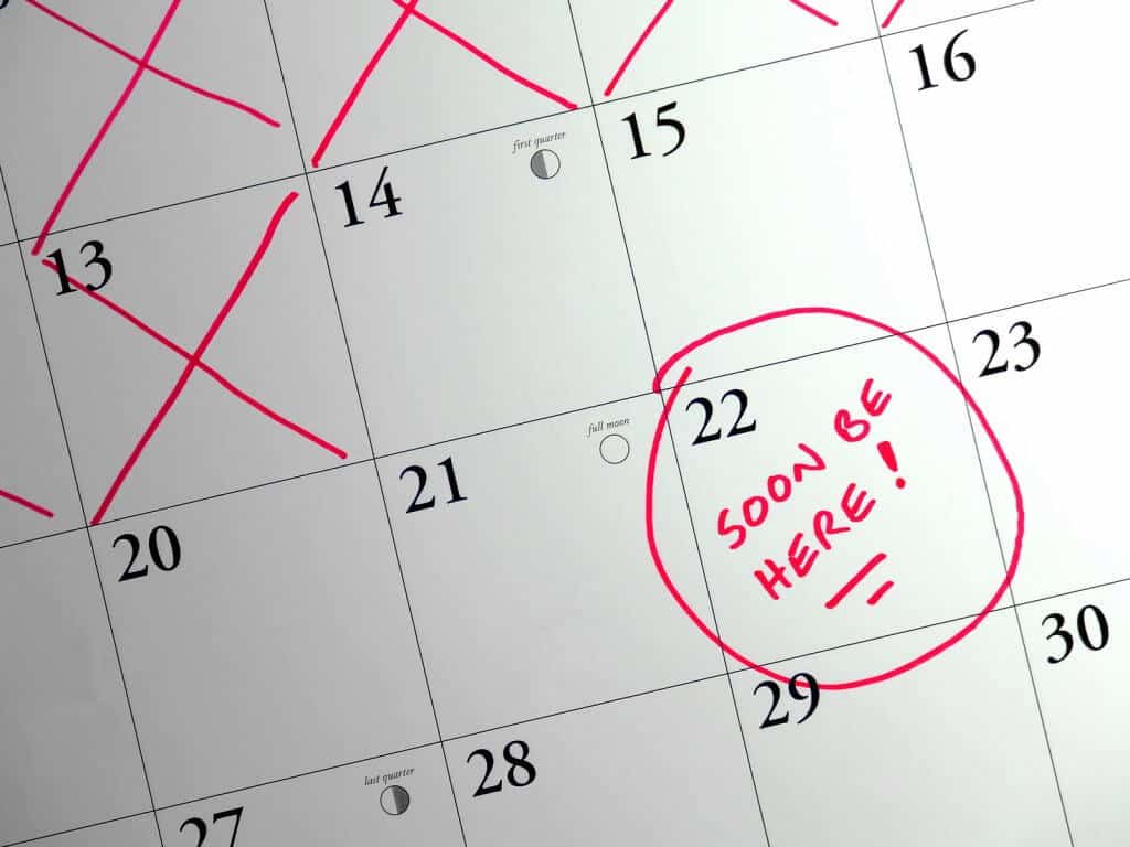 Close-up of a calendar with days crossed off and one date circled and noted with "soon be here" in red ink.