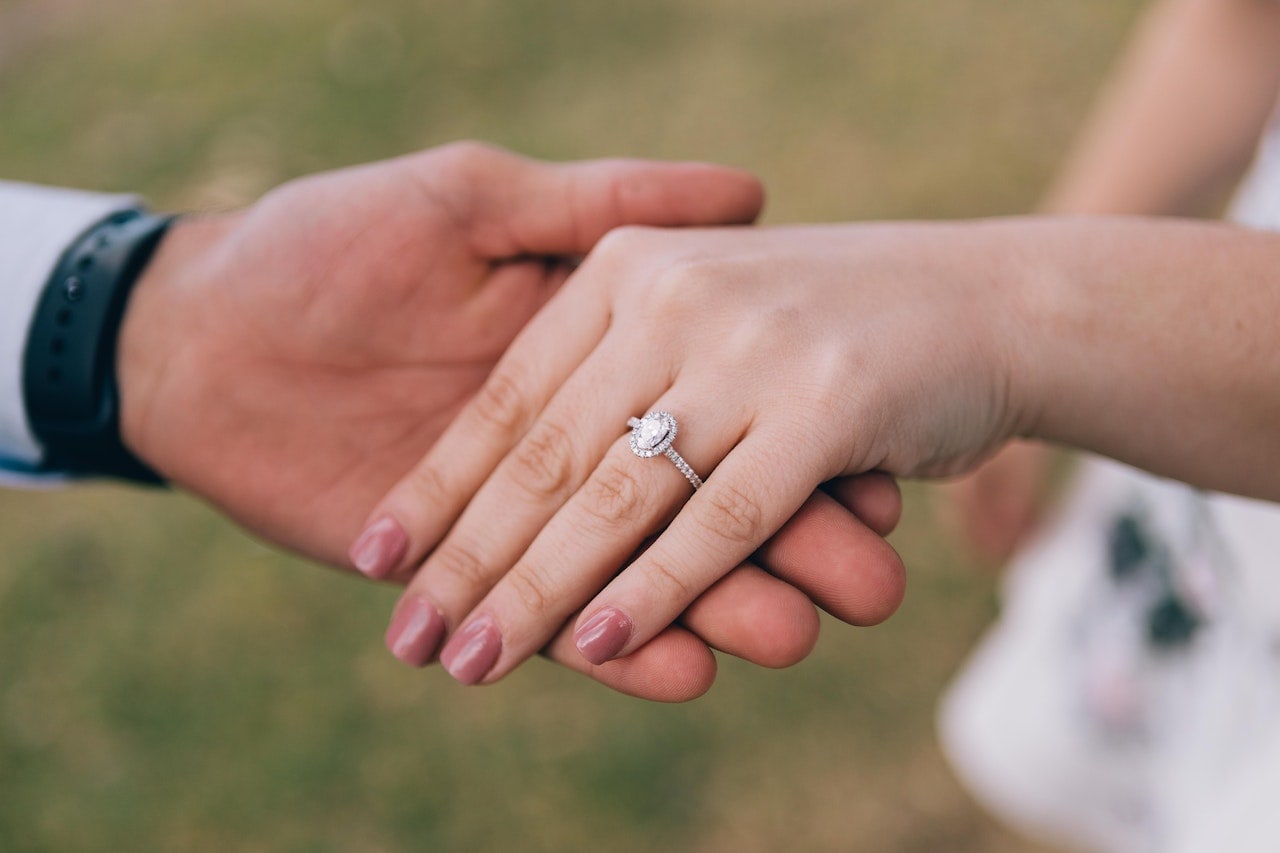 man and woman holding hands with oval diamond ring