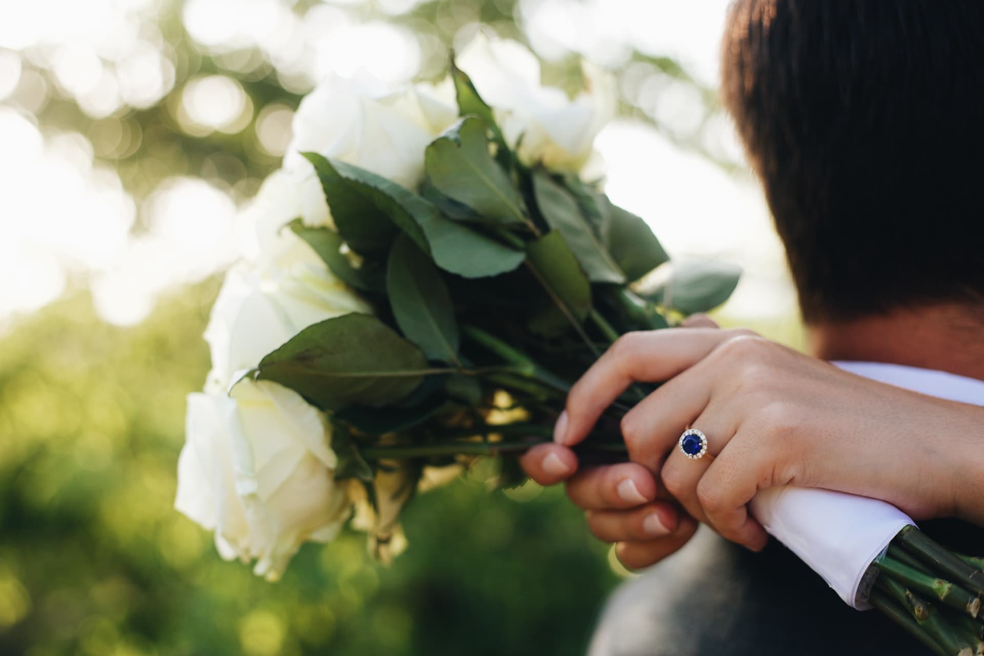 blue sapphire ring on finger with white roses