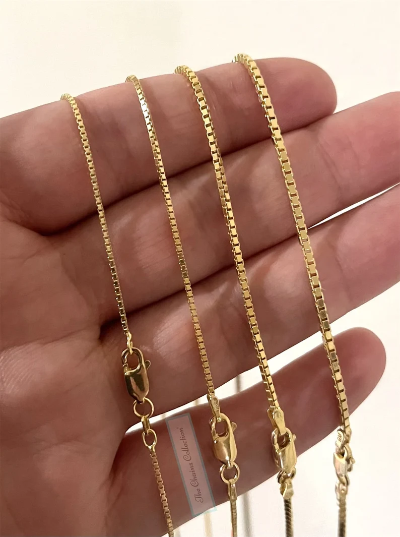 a hand holding four gold box chain necklaces