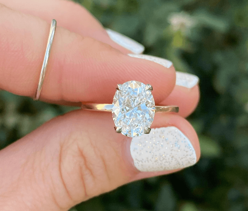 fingers holding an oval cut diamond ring