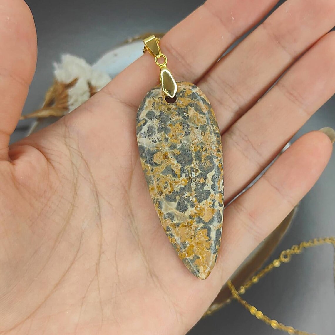 a hand holding leopardskin jasper pendant with gold chain