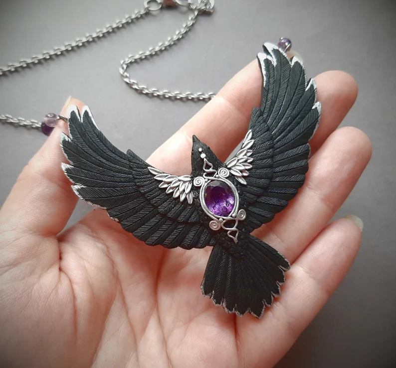 a hand holding raven crow halloween necklace